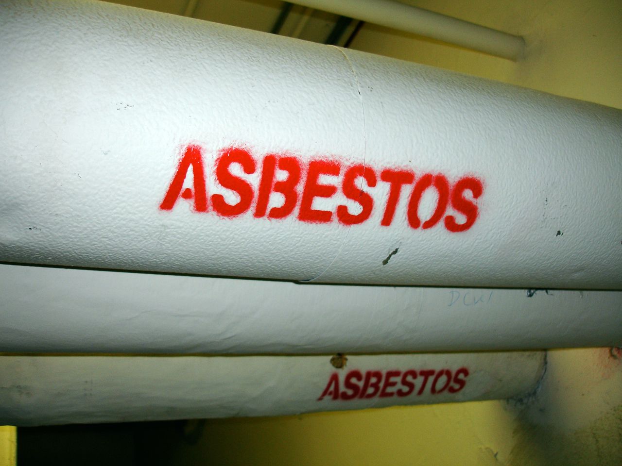 Canos com isolamento de amianto, sinalizados com o aviso "ASBESTOS" (amianto, em inglês).